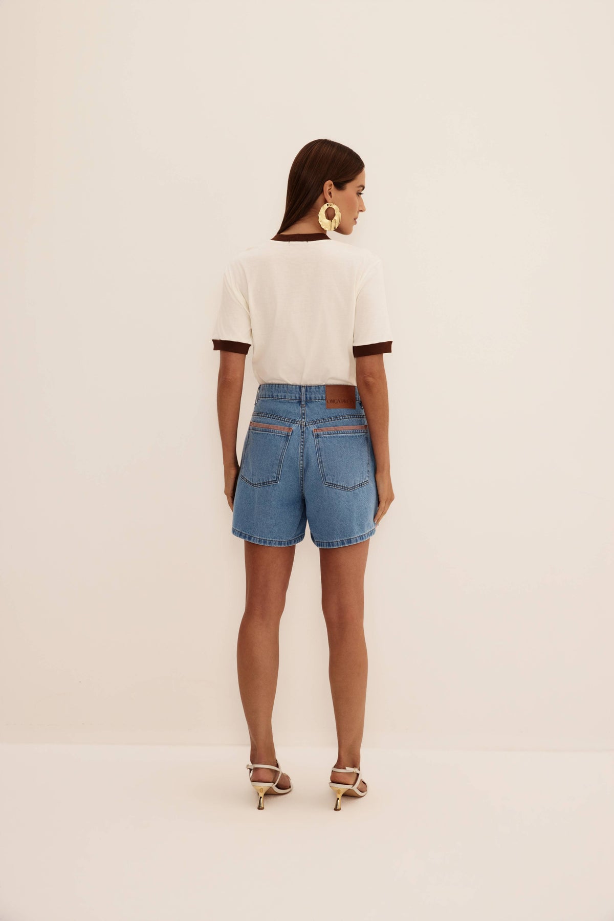 Bermuda jeans azul com costas lisas, bolsos traseiros com detalhe marrom e etiqueta, vista de costas