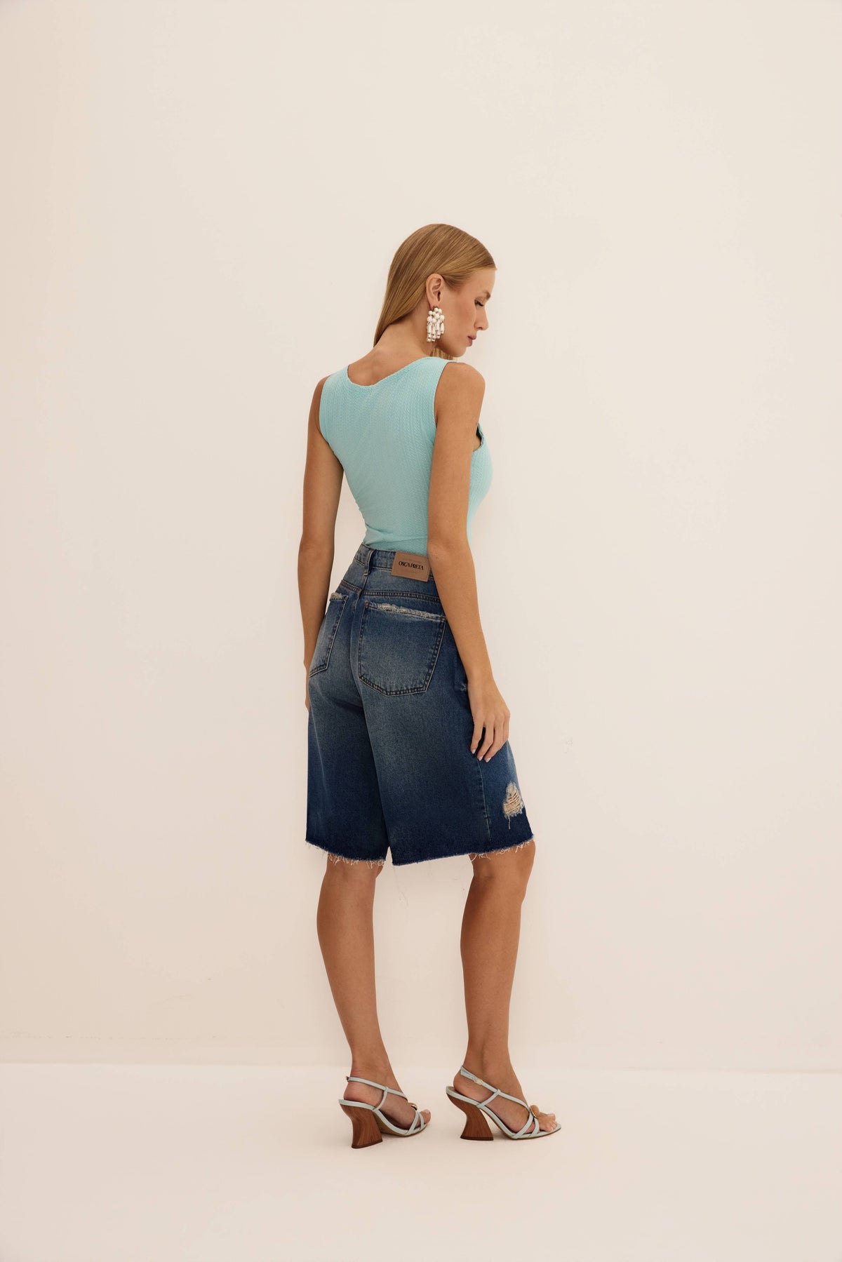 Bermuda tradicional jeans vista de costas, com bolsos traseiros, etiqueta de couro e barra desfiada