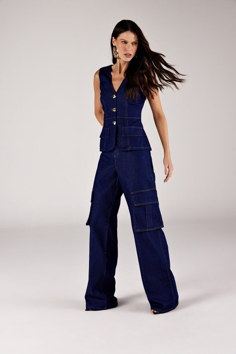 Calça reta jeans bolsos cargo azul escuro, look de frente em movimento com colete jeans Onça Preta