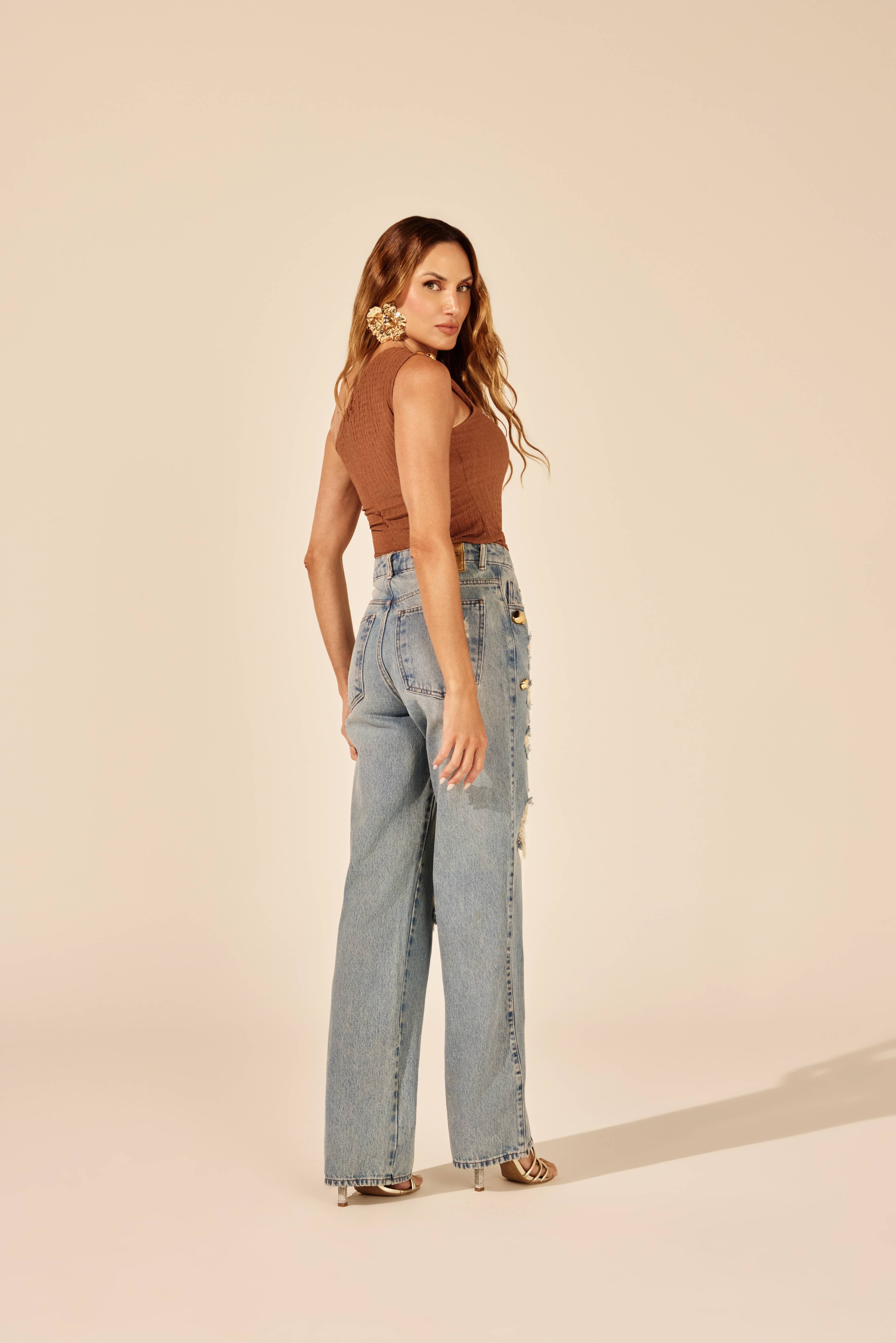 Calça reta jeans rasgada tachas douradas azul clara, vista traseira com body caramelo Onça Preta