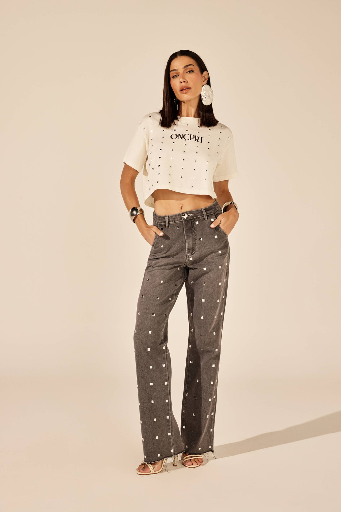 Calça jeans cinza reta com tachas metálicas, look de frente com t-shirt Onça Preta