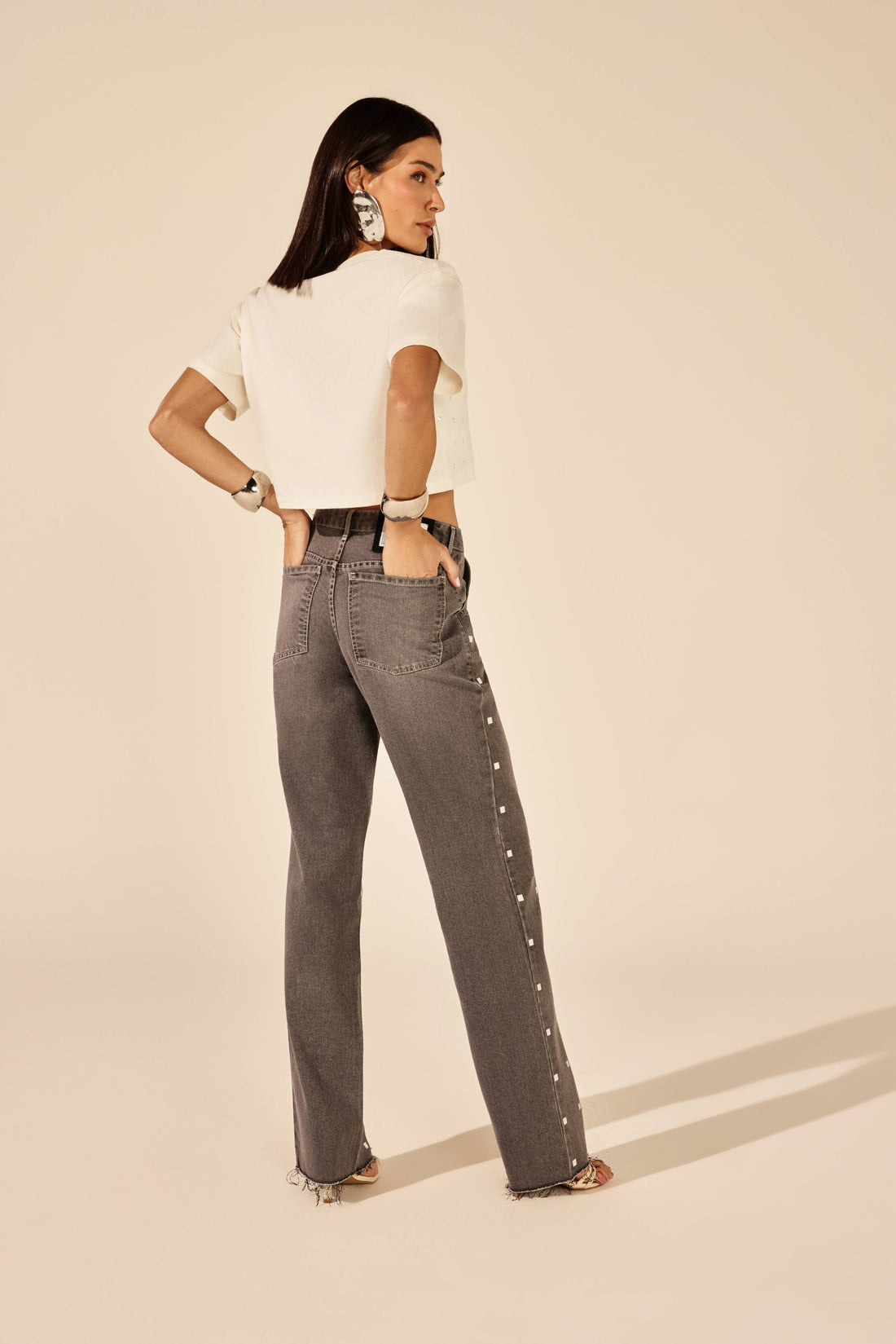 Calça jeans cinza reta com tachas metálicas, look de frente com t-shirt Onça Preta