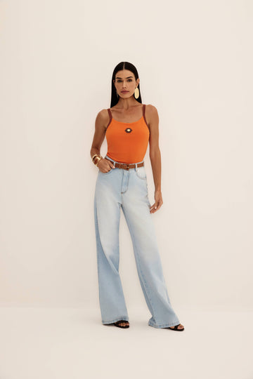 Calça jeans wide leg de lavagem clara com cintura alta e perna ampla, vista de frente com regata laranja