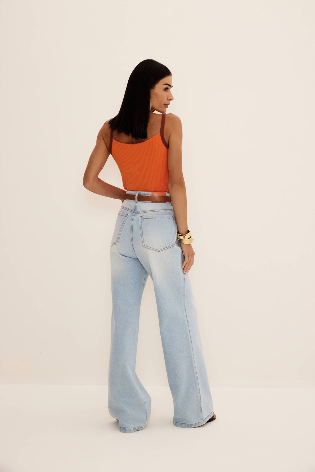 Calça jeans wide leg de lavagem clara com cintura alta e perna ampla, vista de frente com regata laranja