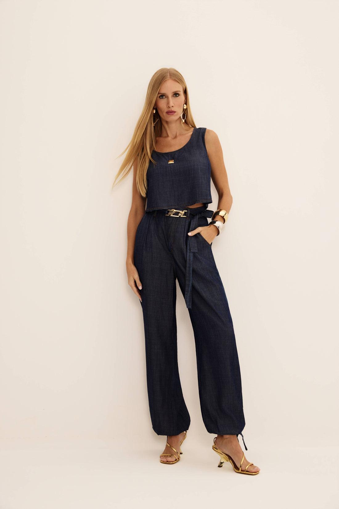 Calça jeans aladim azul escura com pregas, cintura alta e amarração na barra, vista de frente