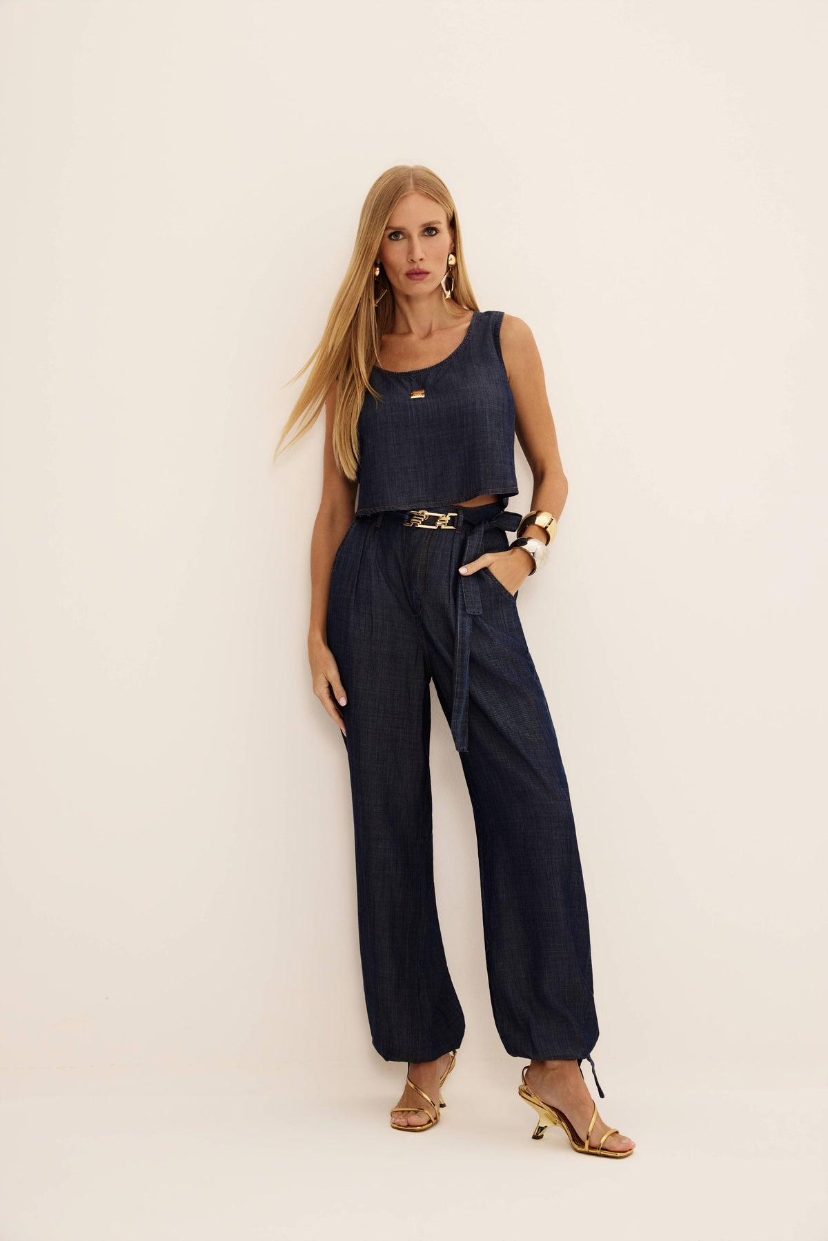 Calça jeans aladim azul escura com pregas, cintura alta e amarração na barra, vista de frente