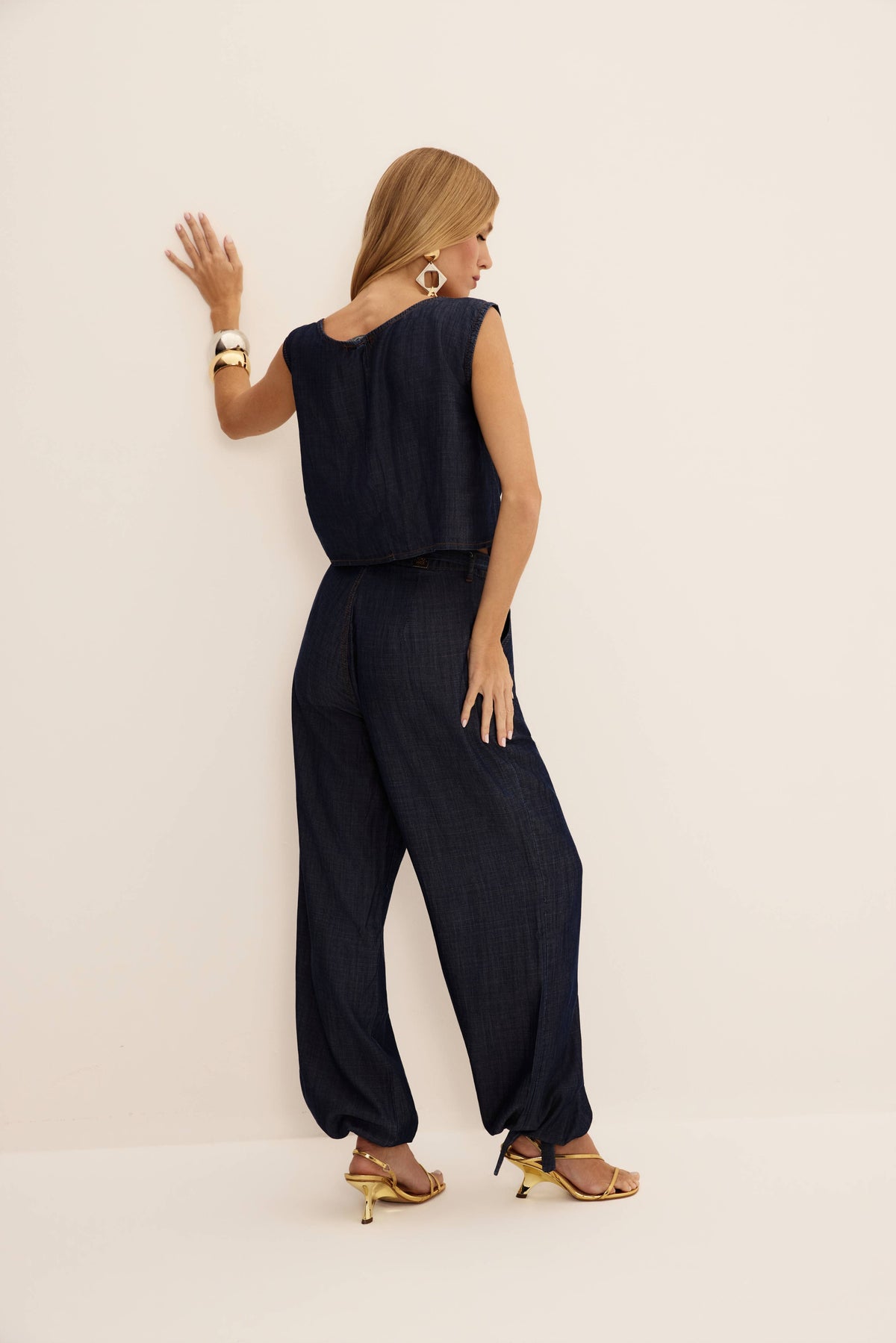 Calça jeans aladim azul escura com caimento fluido e amarração na barra, vista de costas
