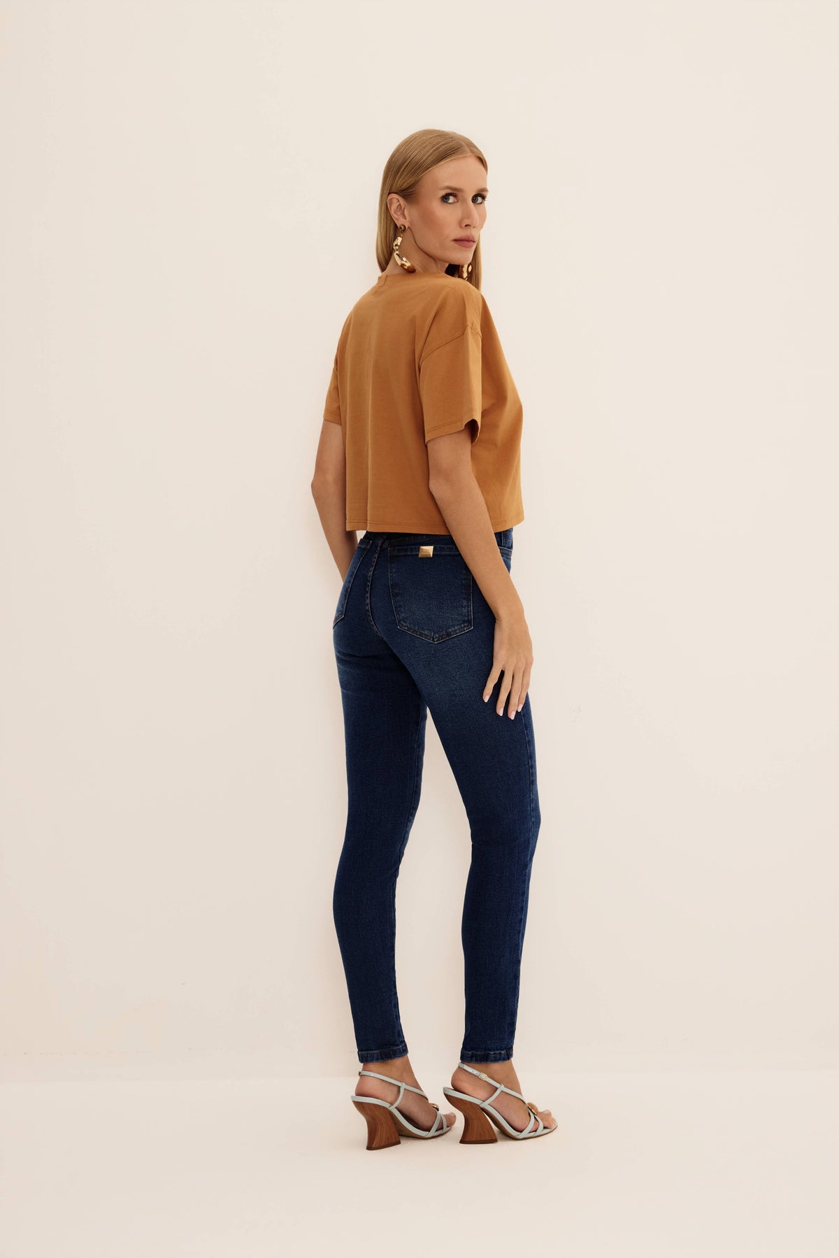 Calça jeans skinny azul escura com bolsos traseiros e placa metálica, vista de costas