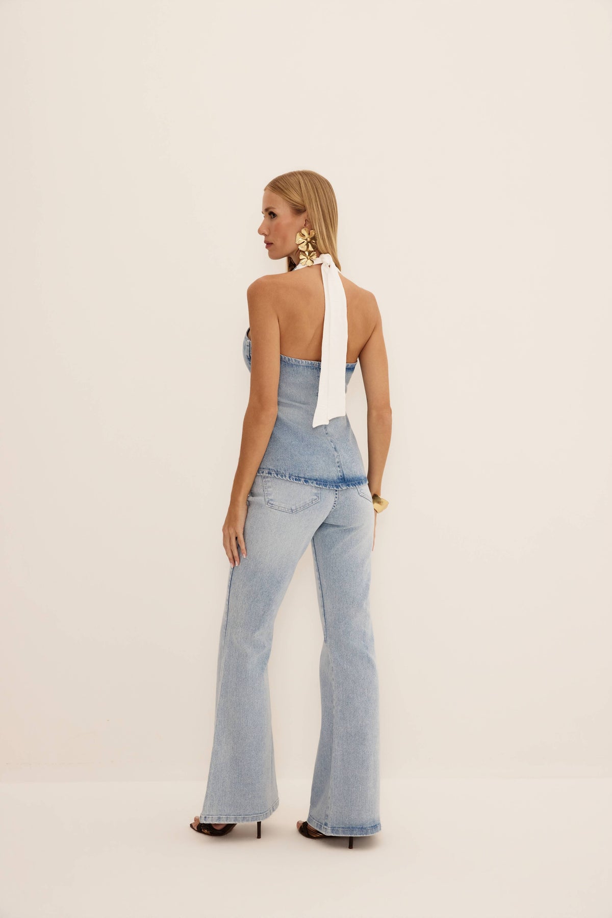 Calça flare básica jeans claro vista de costas, com bolsos traseiros e boca ampla até o chão