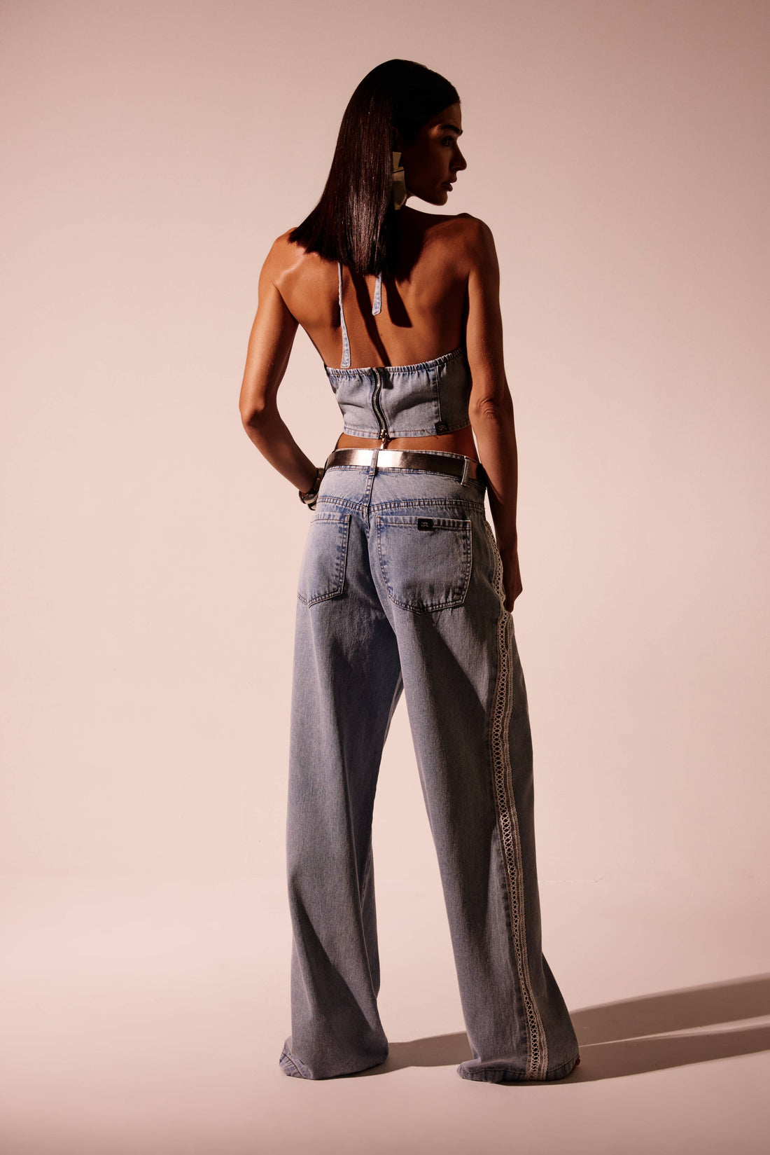 Calça jeans reta clara com perna ampla e detalhe lateral em macramê, vista de frente com cinto