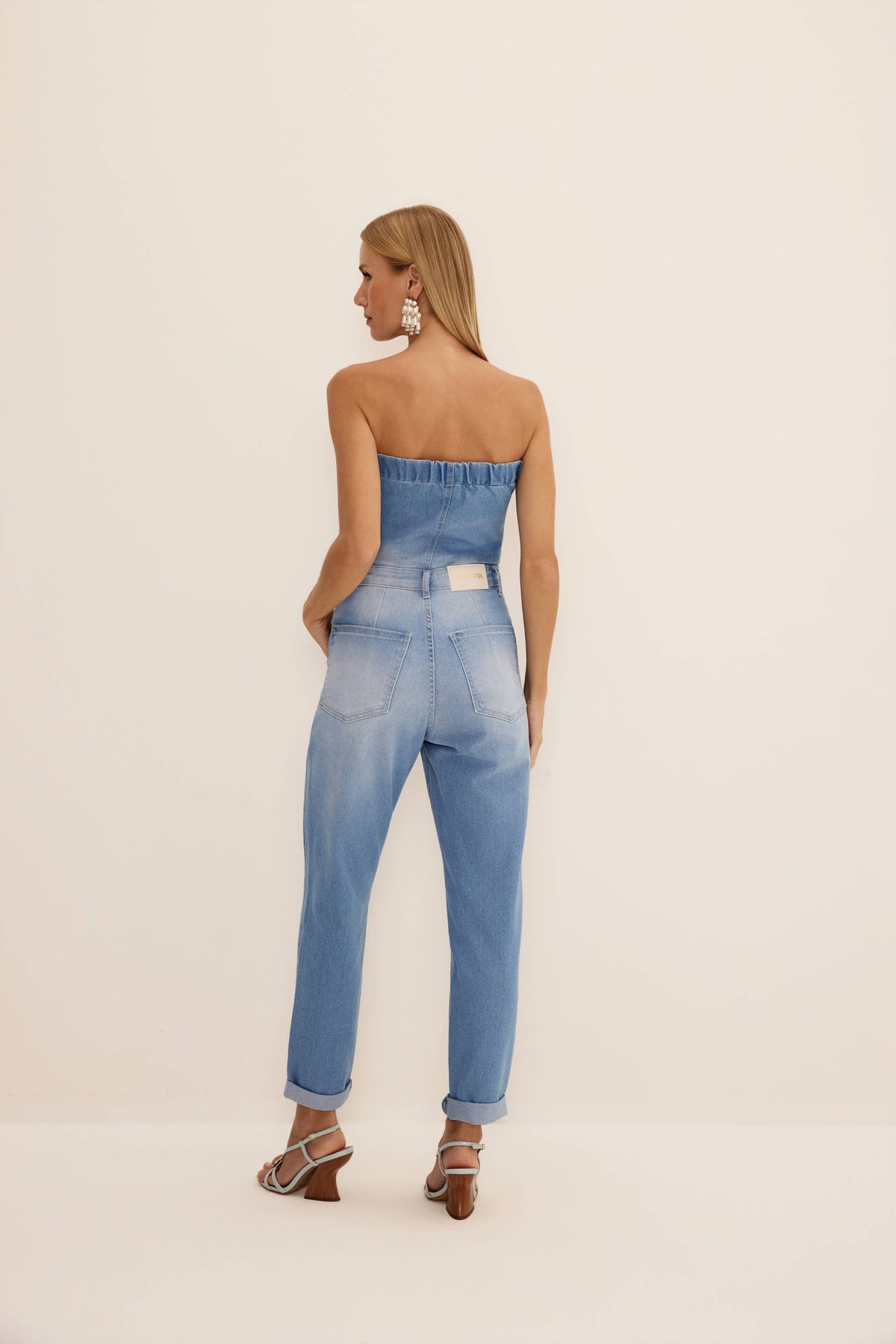 Macacão mom tomara que caia jeans visto de costas, com elástico no busto, bolsos traseiros e barra dobrada
