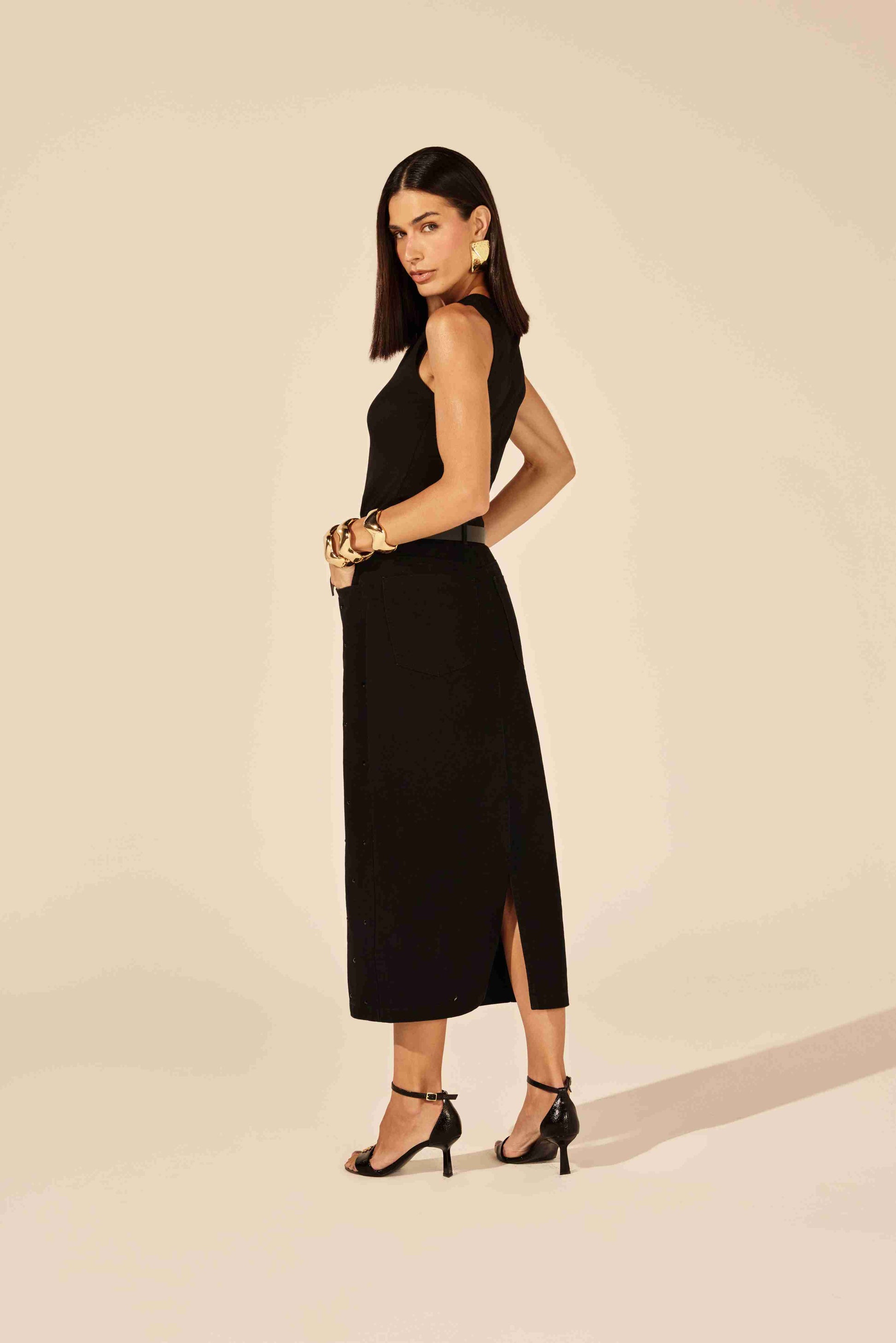 Saia midi jeans preta com detalhes brilhantes de strass, modelagem justa, em fundo neutro Onça Preta.

