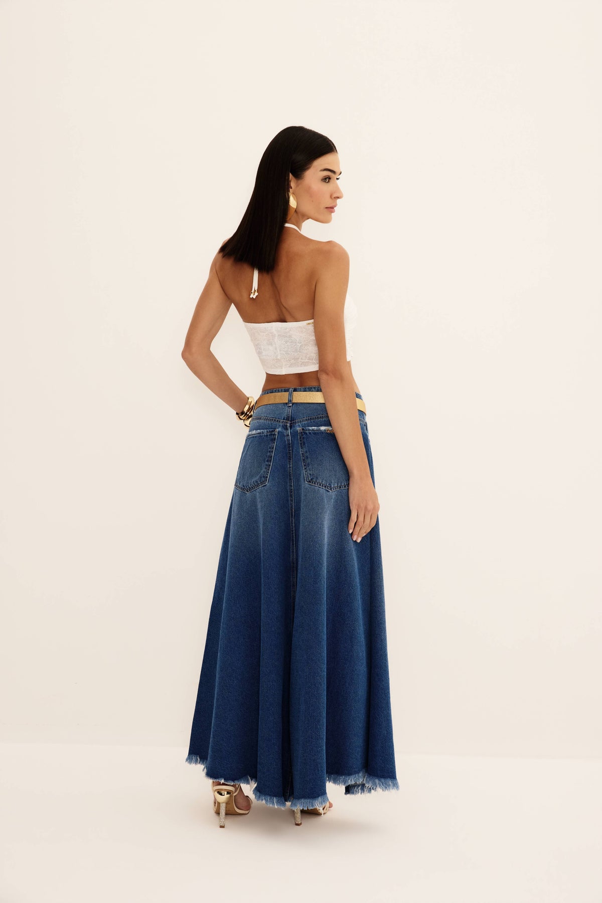 Saia jeans longa azul evasê com bolsos traseiros e barra desfiada, vista de costas