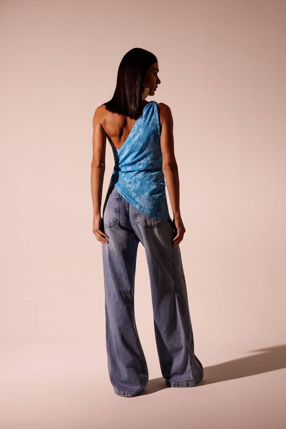 Blusa ombro único azul com corrente dourada e amarração lateral, look frontal com calça wide leg jeans Onça Preta