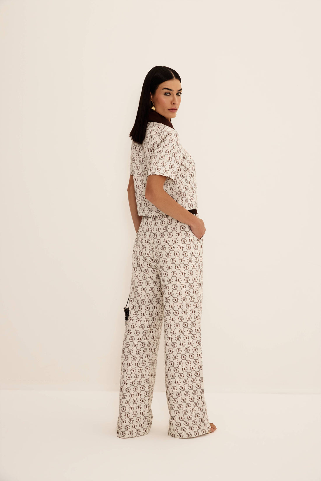 Camisa cropped logomania marrom fundo cru com gola e vista em contraste, look frontal com calça da mesma estampa Onça Preta