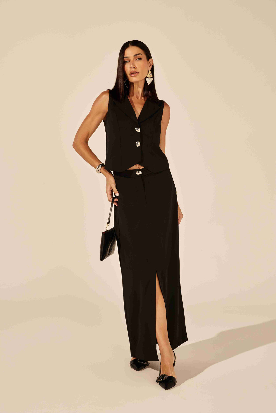 Colete de alfaiataria feminino básico preto - modelo vestindo colete com calça e blusa off-white, em ambiente urbano Onça Preta.