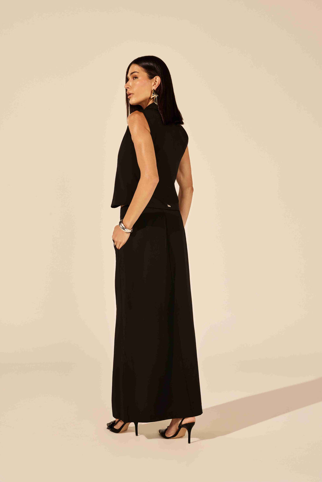 Colete de alfaiataria feminino básico preto - modelo vestindo colete com calça e blusa off-white, em ambiente urbano Onça Preta.