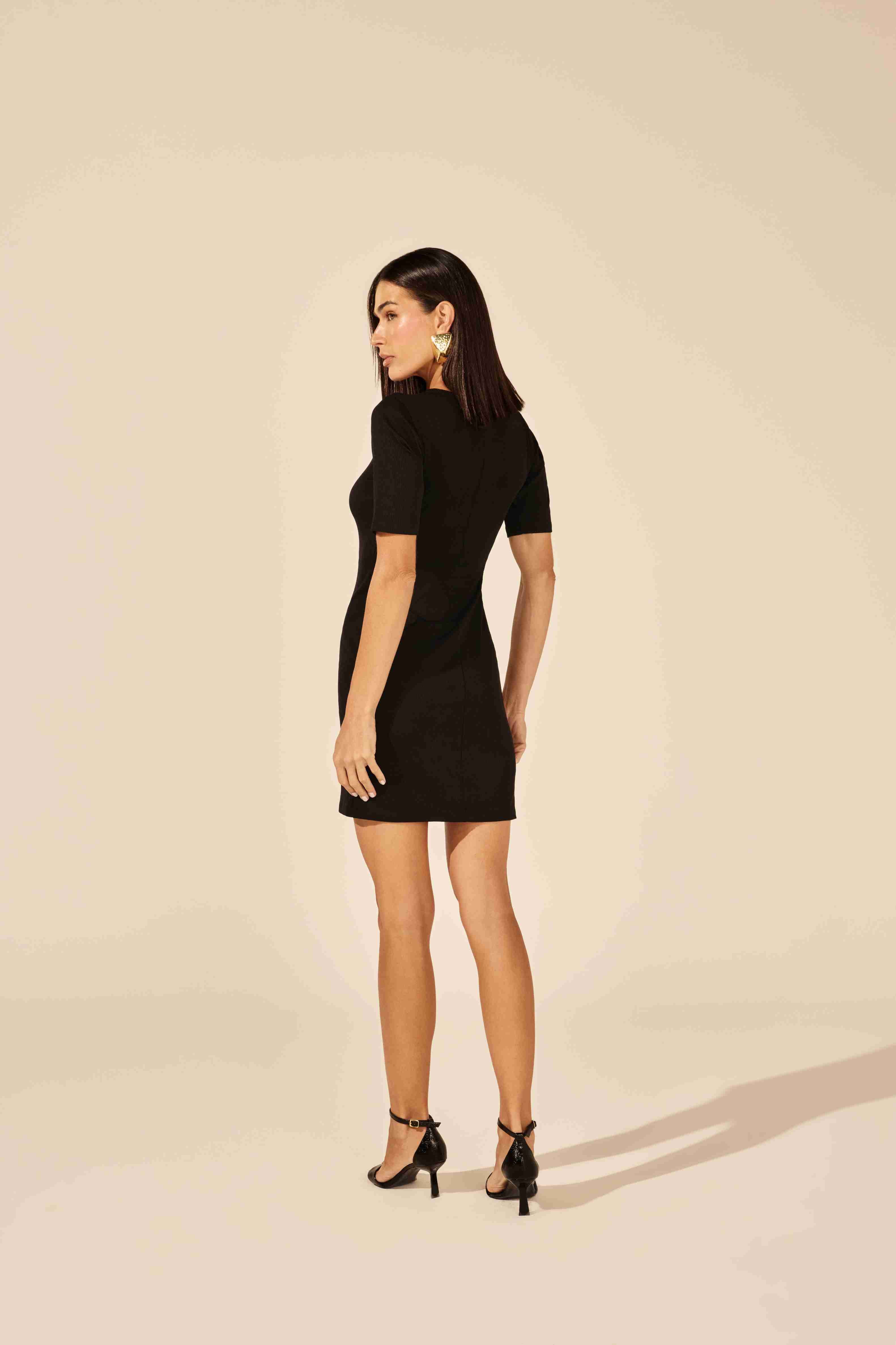 Vestido curto decotado etiqueta frontal preto - modelo posando com confiança em evento noturno Onça Preta
