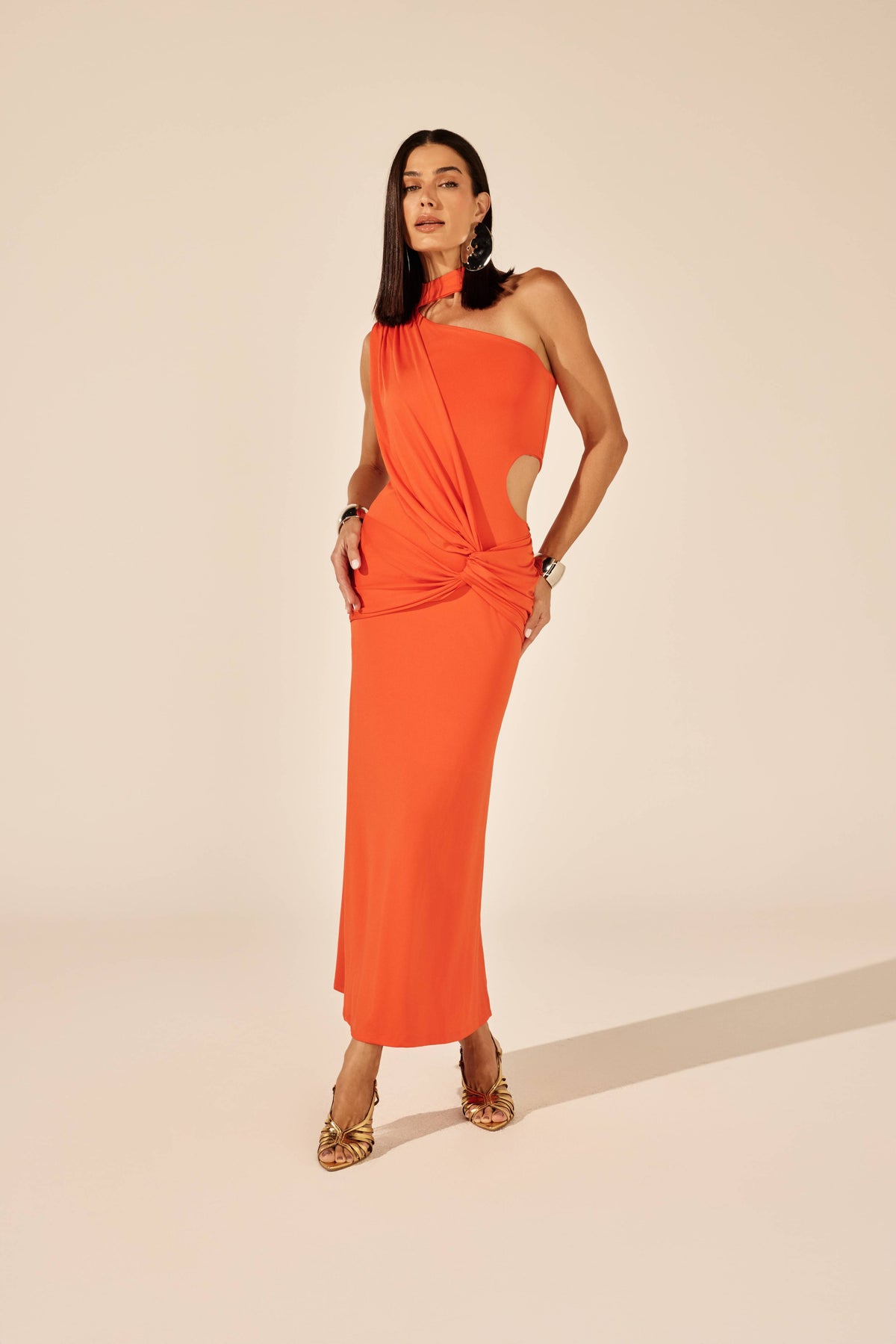 Vestido midi franzido laranja com cut out e nó frontal, look de frente com sandália dourada Onça Preta