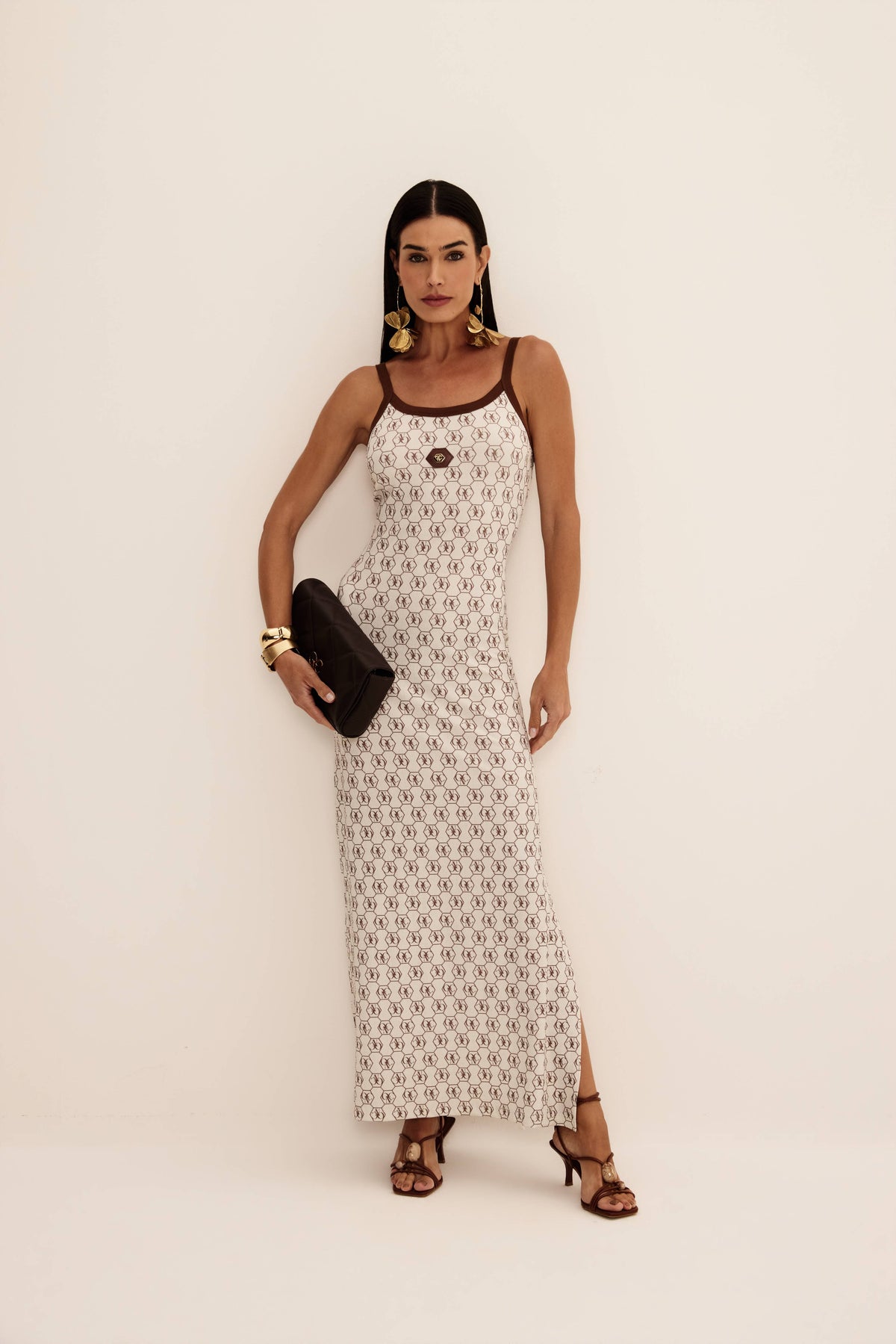 Vestido super midi regata logomania marrom fundo cru com viés em contraste e fenda lateral, look frontal com clutch preta Onça Preta