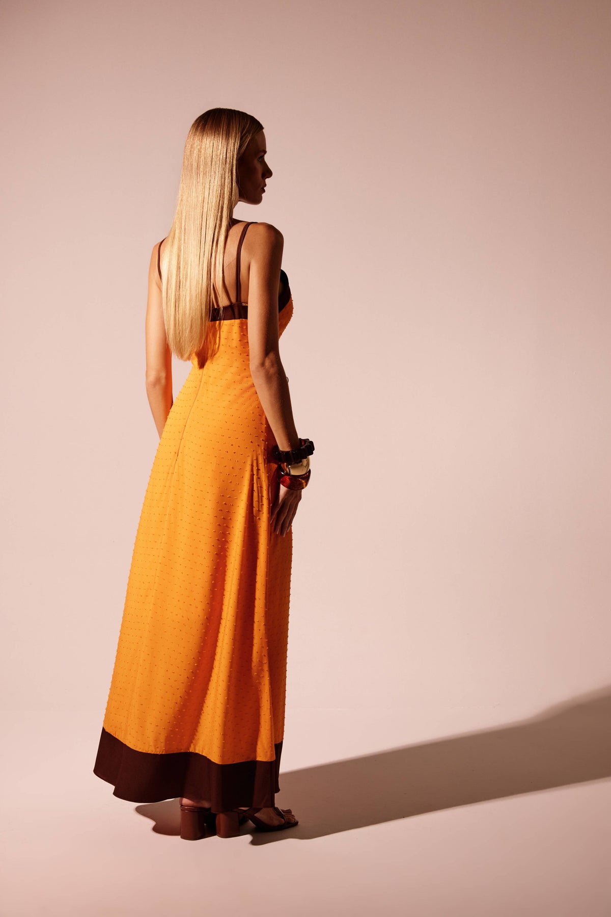 Vestido longo laranja com barra em contraste, vista de costas mostrando zíper central e detalhe metálico
